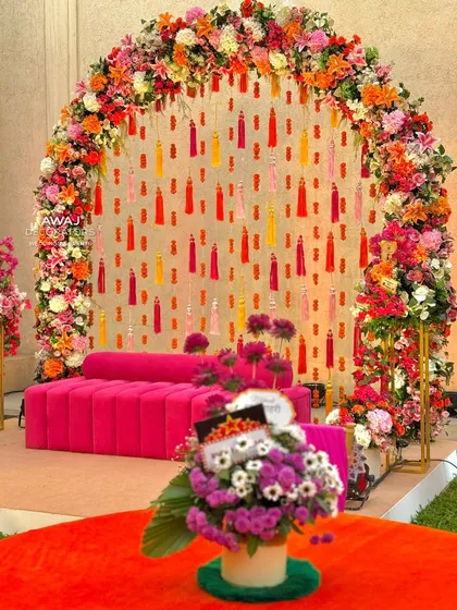 A glimpse into a vibrant Mehendi ceremony, featuring a beautiful floral arch and bright pink seating, creating a festive and picture-perfect spot for the bride.