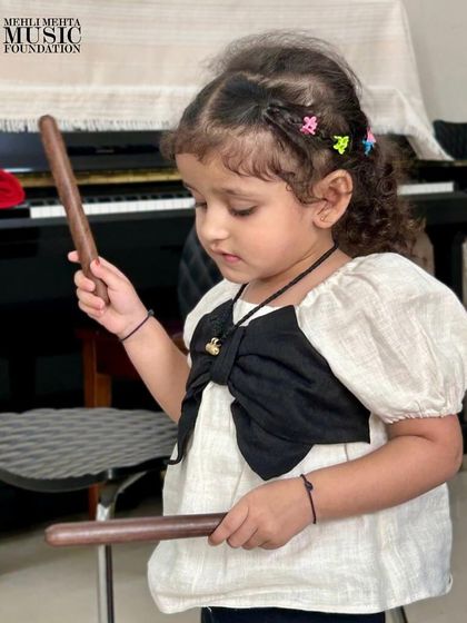 A young child discovers the sound of claves. Hands-on experience with instruments is fundamental to our teaching approach for early learners.