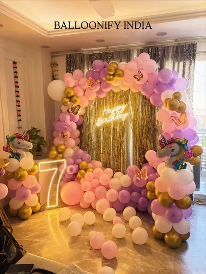 We brought a unicorn dream to life for this 7th birthday party. This popular theme features a circular balloon arch in pastel pink, purple, and gold, a 'Happy Birthday' neon sign, and a large light-up number '7'. The unicorn balloon pillars on each side complete the magical look.