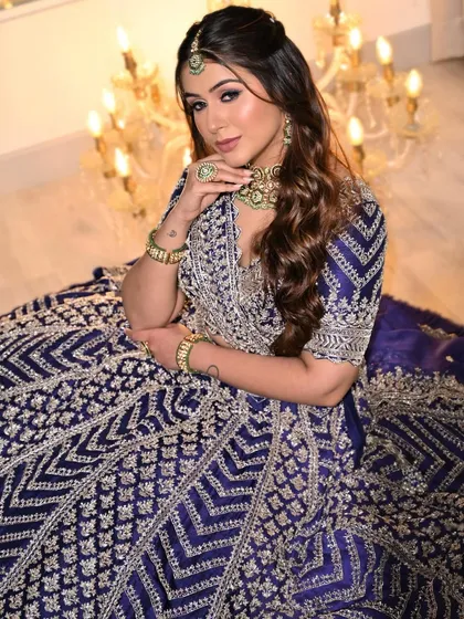 A regal seated portrait showcasing the full festive ensemble. The deep blue lehenga and dramatic makeup create a look that is fit for a modern queen.