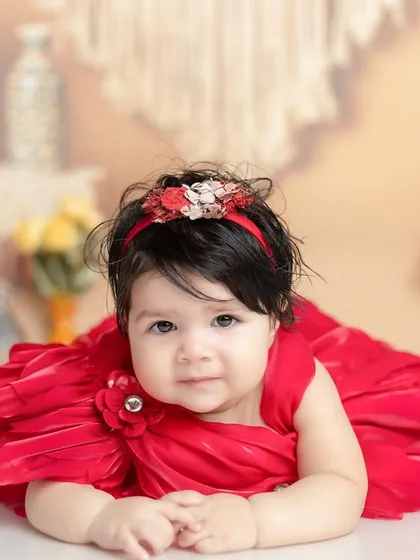 A beautiful six-month-old baby girl in a stunning red dress. The soft, bohemian-style background adds warmth without being distracting.