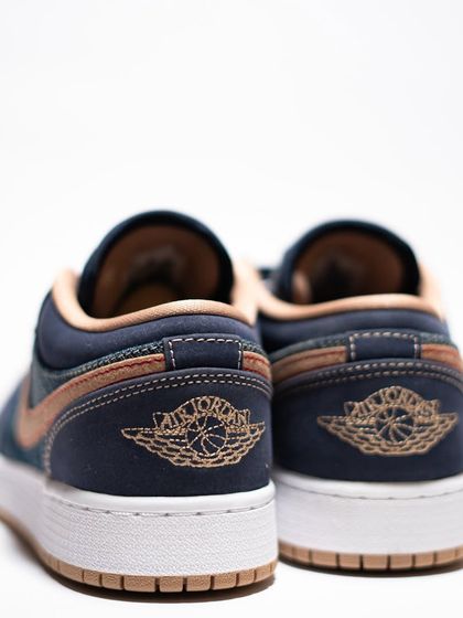 The heel view of the Jordan 1 Low 'Denim', featuring the iconic Air Jordan Wings logo stitched in a contrasting tan thread.