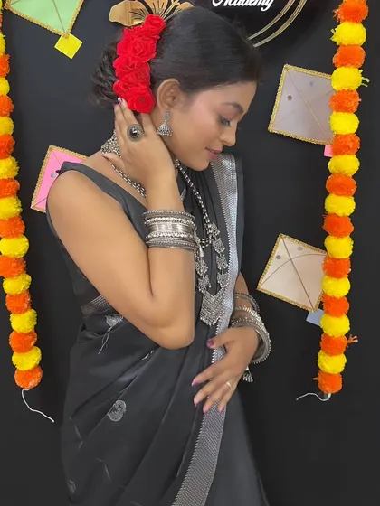 A side profile of the Makar Sankranti look, showing the elegant bun with red roses and the layered silver necklaces.