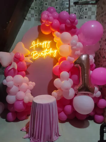 The same pink first birthday setup, now with a 'Happy Birthday' neon sign and a small table for the cake.
