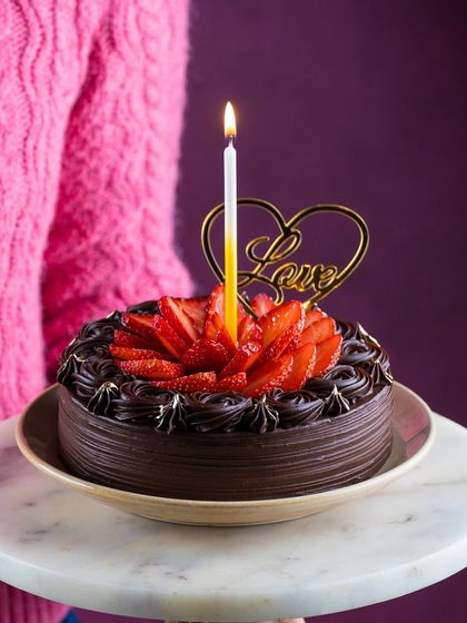 A classic chocolate strawberry cake held up for a Valentine's celebration. The simple 'Love' topper and fresh strawberries make it a perfect romantic gesture.