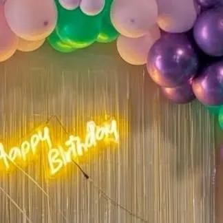 A close-up of a 'Happy Birthday' neon sign against a shimmery backdrop, a perfect add-on to make any birthday decoration stand out.