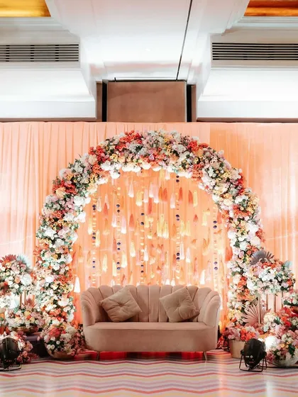 A beautiful pastel Haldi decor setup. The focal point is a floral arch in soft peach tones, creating an elegant and dreamy photo corner for the couple and their guests.