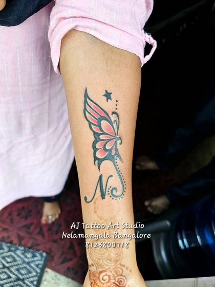 A butterfly tattoo with a star and the initial 'N' woven into the design.
