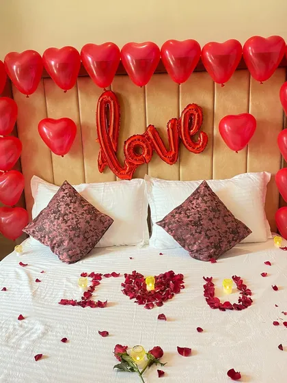 The full view of the romantic bed decoration, combining a "Love" foil balloon, heart balloons, and rose petals.