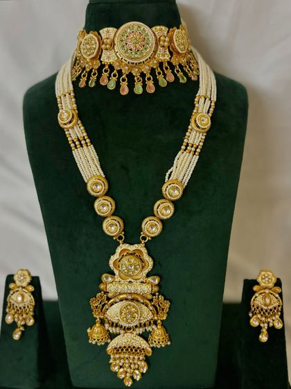This rental set features a choker with delicate pink and green Meenakari work, paired with a long pearl necklace with a grand pendant.