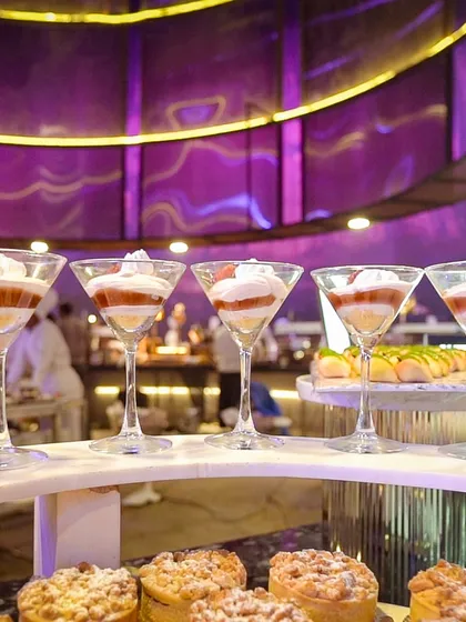 A row of elegant dessert glasses filled with layered trifles, displayed on a curved, modern dessert bar.