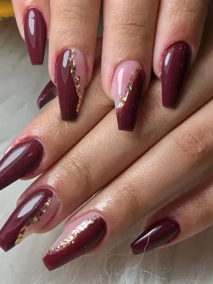 A sophisticated design with coffin-shaped nails, combining a deep maroon polish with a diagonal color block and gold foil accents.