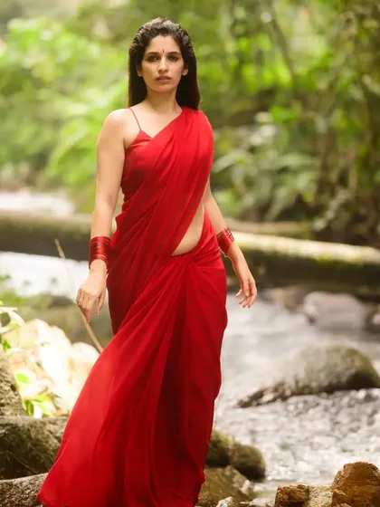 "Baanadi mooduva kalarava naanu!" I am the chirping that rises in the sky. For this outdoor portrait, we used the natural forest stream as a backdrop, letting the vibrant red saree stand out against the greens. This shot is all about capturing a story of being one with nature.