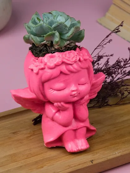 This sweet angel planter is perfect for a small succulent. The vibrant pink color and serene expression make it a charming addition to a desk or shelf.