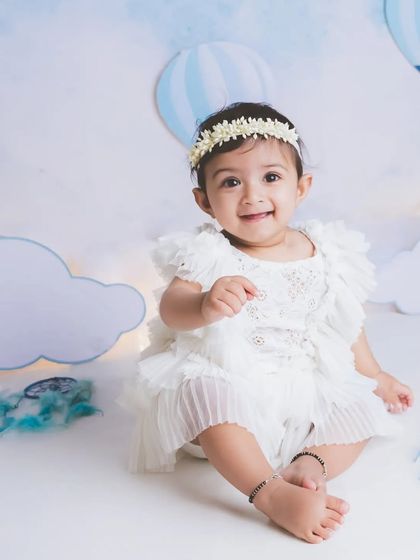 A sweet baby girl in a simple white dress against a dreamy blue sky and cloud background. This setup is perfect for creating a whimsical and angelic feel.