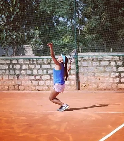 A player demonstrates excellent form during her serving motion on the clay court. I work closely with advanced students to refine every aspect of their game, including powerful and consistent serves.