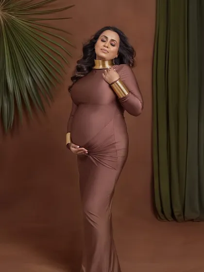 A classic maternity pose, cradling the bump, elevated by the unique styling and rich, earthy tones.