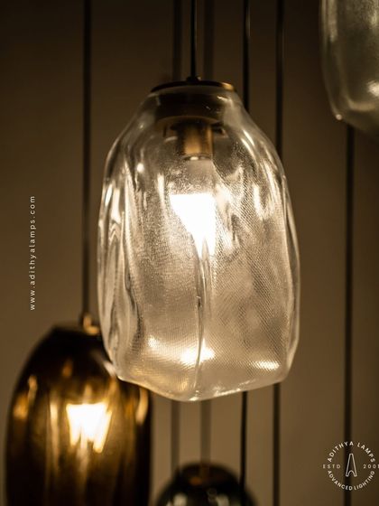 This cascading installation features pendants made of organic, free-form glass in smoked and amber tones. The textured, irregular shapes create a beautiful, water-like effect, perfect for adding a sense of calm and artistry to a room.