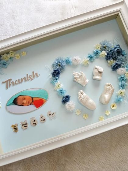 For baby Thanish, I created this heart-shaped floral arrangement using blue and white flowers around his pure white casts. The design includes his photo and birth details, all within a clean white frame.