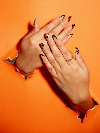 Breaking through with a bold design. This look features a black and gold leopard print on long, pointed nails, creating a fierce and glamorous statement. The way the hands break through the paper adds a cool, edgy vibe.