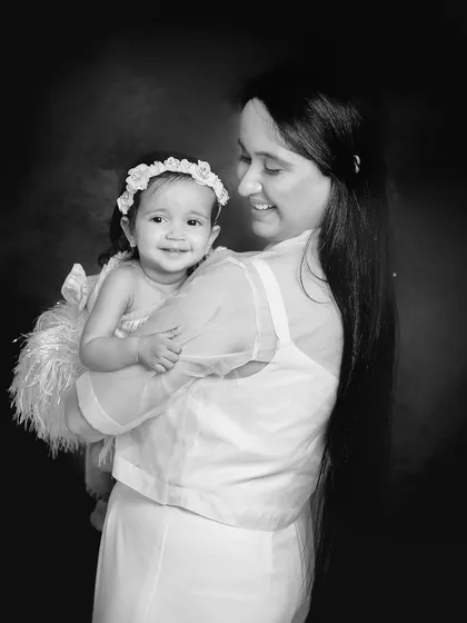 A beautiful black and white photo of a mother holding her young daughter. The dark background and soft lighting create an intimate and artistic portrait.