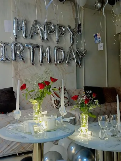 A romantic birthday surprise at home, with "Happy Birthday" foil balloons, red roses, and candles creating a warm and loving atmosphere.
