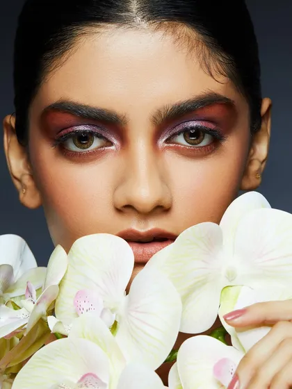 A dramatic, smokey eye with deep purple and red tones, complemented by the soft petals of white orchids.