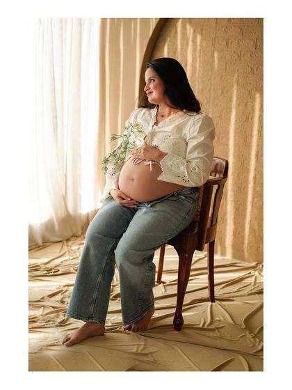 A seated portrait of the mother-to-be in a casual outfit, looking serene and beautiful by the window.