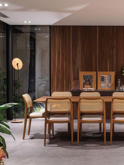 This dining area demonstrates how we use plants to soften modern interiors. A large potted plant is placed by the window, complementing the natural wood and rattan textures of the furniture and creating a warm, inviting atmosphere.