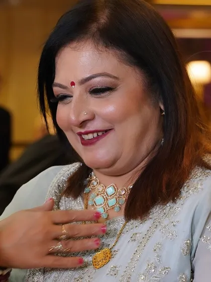 A candid, happy shot of a mother at a wedding function. Her makeup is fresh and radiant, with a lovely pop of color on her lips.