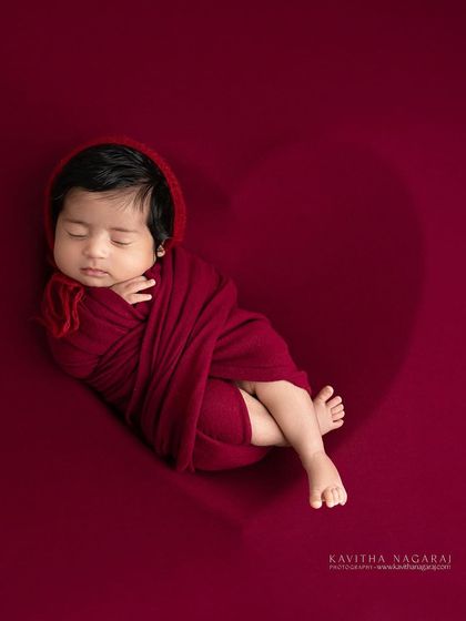 A newborn rests peacefully, nestled inside a heart-shaped outline on a rich red background. A simple and beautiful way to say "welcome to the world."
