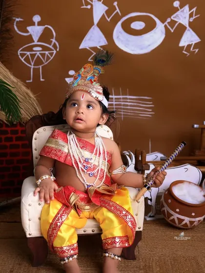 A regal pose from our little Krishna. Seated on a miniature throne, he holds a flute, looking every bit the part in this beautifully styled Janmashtami photoshoot.