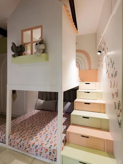 This is the full view of the custom house-shaped bunk bed I designed. The stairs leading to the upper loft have built-in drawers for clever toy storage, and the pastel colors keep the room feeling light and cheerful.