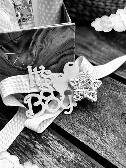 An artistic, black and white shot capturing the "It's a Boy" tag and delicate star accent from the dino-themed hamper, highlighting the fine details and textures.