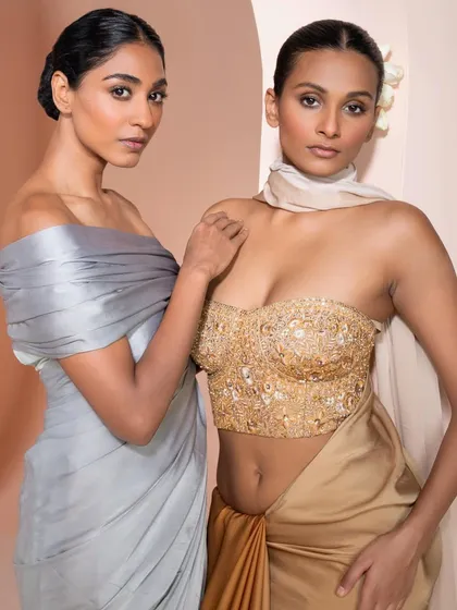 Two distinct yet harmonious looks. One model wears a draped grey satin gown, while the other stuns in a gold embroidered bustier, showcasing different facets of modern occasion wear.