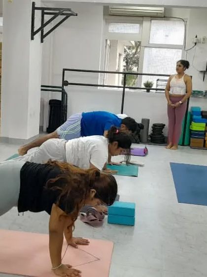 Our instructor watches over the class as they hold Phalakasana (Plank Pose), offering verbal cues to maintain strong form.