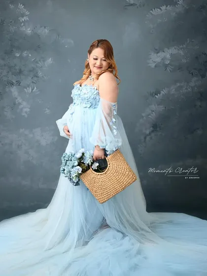 A dreamy and soft portrait in a pastel blue gown. The painted backdrop and the gentle pose create a whimsical, fairytale-like quality.