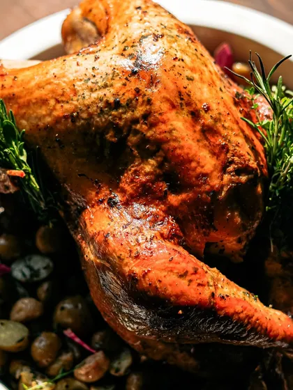 A detailed shot of the roasted turkey, highlighting the texture of the skin and the fresh herbs. Our turkeys are cooked to perfection, ensuring a juicy and flavorful result.