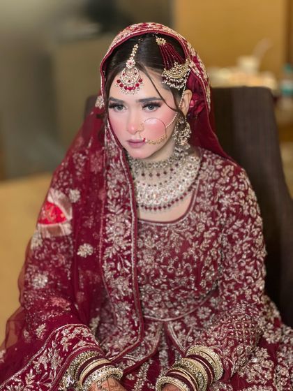 A portrait of a beautiful bride on her Nikkah day. Her makeup features a soft, glowing base with rosy cheeks and defined eyes, complementing her traditional red attire.