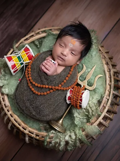 A different angle of the basket pose, this shot captures the baby from the side, highlighting the trishul and damaru props.
