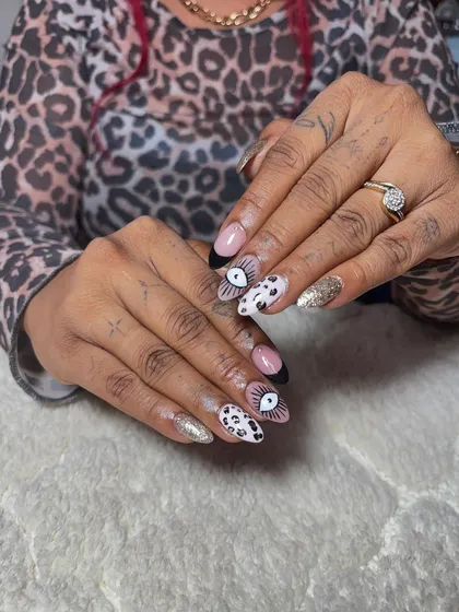 A quirky and artistic set. These almond-shaped nails feature a mix of designs, including an evil eye, dalmatian spots, and glitter accents.