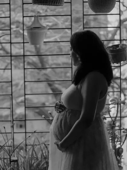 A quiet, contemplative black and white photo of the mother-to-be looking out a window, capturing a moment of peaceful reflection at home.