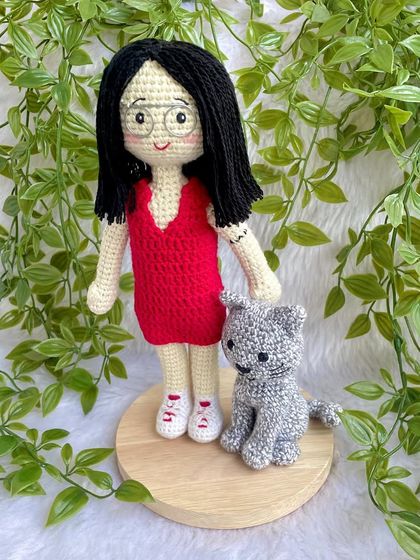 A thoughtful farewell gift for a niece heading off to higher studies. This replica doll in a red dress stands with her pet cat on a display base, a reminder of home she can take with her.