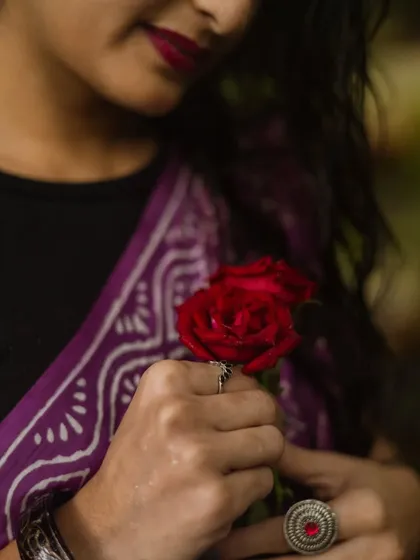 A detail-oriented shot focusing on the hands holding red roses. This image highlights the model's jewelry and the rich color of her saree, telling a story through small, beautiful details.