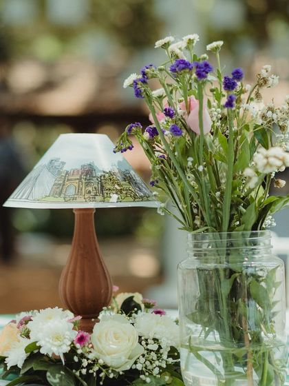 A hand-painted table lamp centerpiece, featuring artwork of local landmarks, sits next to a vase of fresh wildflowers.