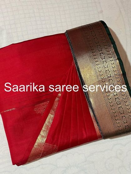 A classic red saree with a dark border, pleated and folded. A timeless piece for any wardrobe.