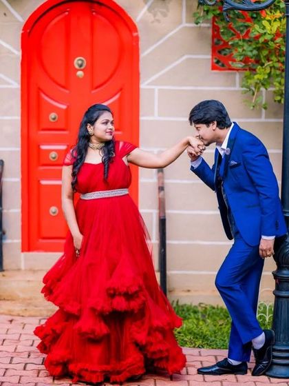 A classic, chivalrous pose for a pre-wedding photoshoot. The vibrant red of the gown pops against the matching red door, creating a visually coordinated and charming picture.