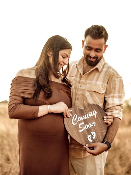 A sweet portrait of the couple looking down at the "Coming Soon" sign they hold over the baby bump, sharing a private, happy moment.
