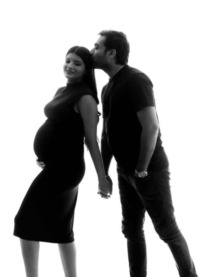A sweet black and white silhouette of a couple holding hands, with the dad-to-be placing a gentle kiss on his partner's forehead.