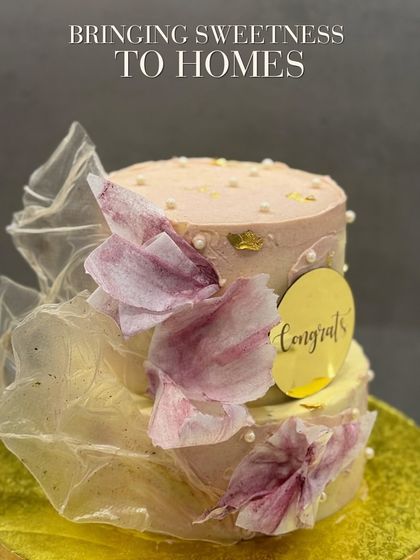 A two-tiered "Congrats" cake designed with soft, ethereal textures. The cake is wrapped in translucent, edible fabric and adorned with delicate, hand-painted floral elements and small pearls for a touch of elegance.